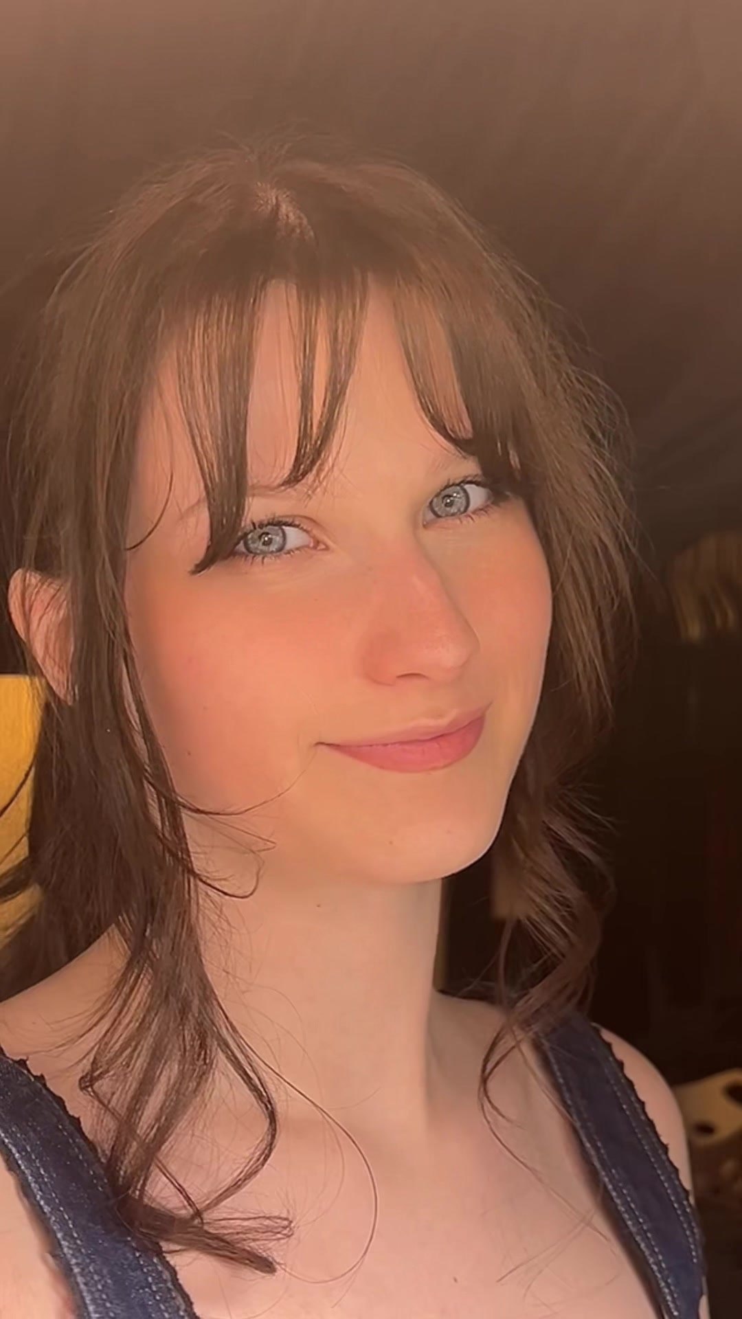 Persephone smiling in warm light, wearing denim overalls